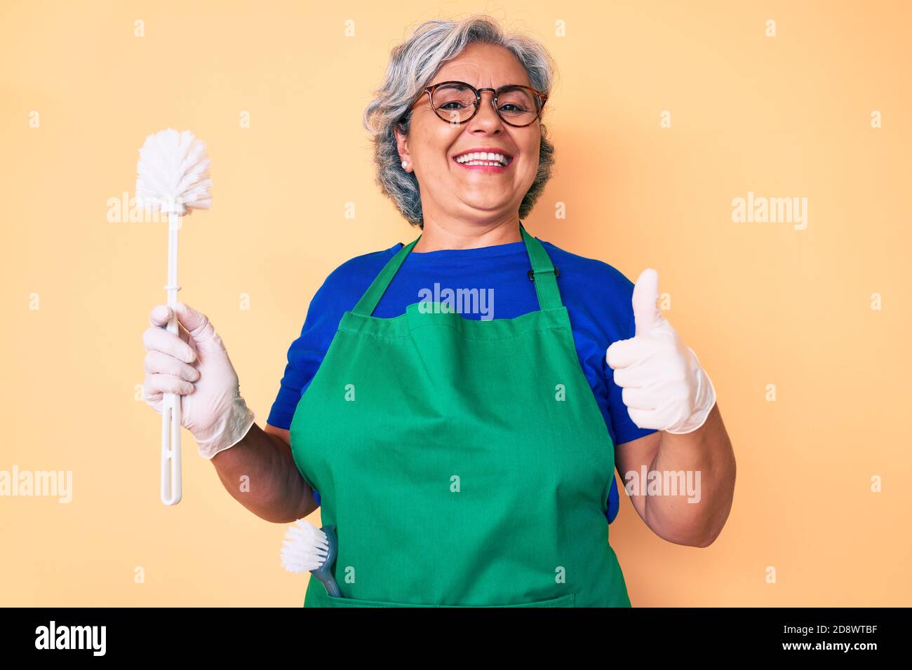 Senior hispanic woman wearing apron holding brush smiling happy and ...