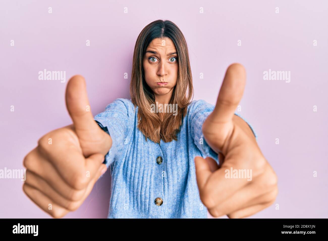 Brunette young woman doing thumbs up positive gesture puffing cheeks with funny face. mouth inflated with air, catching air. Stock Photo