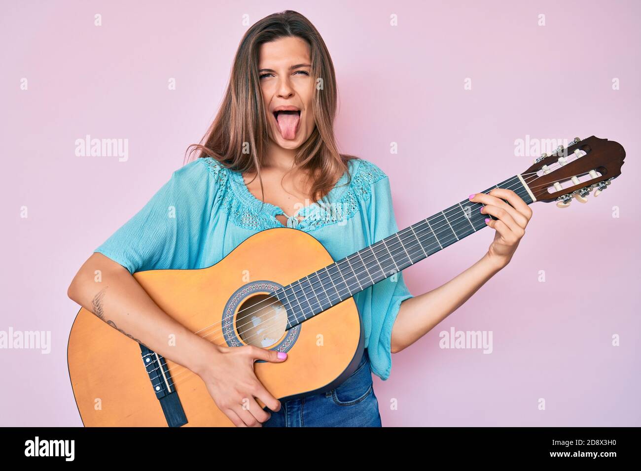 Beautiful caucasian woman playing classical guitar sticking tongue out happy with funny