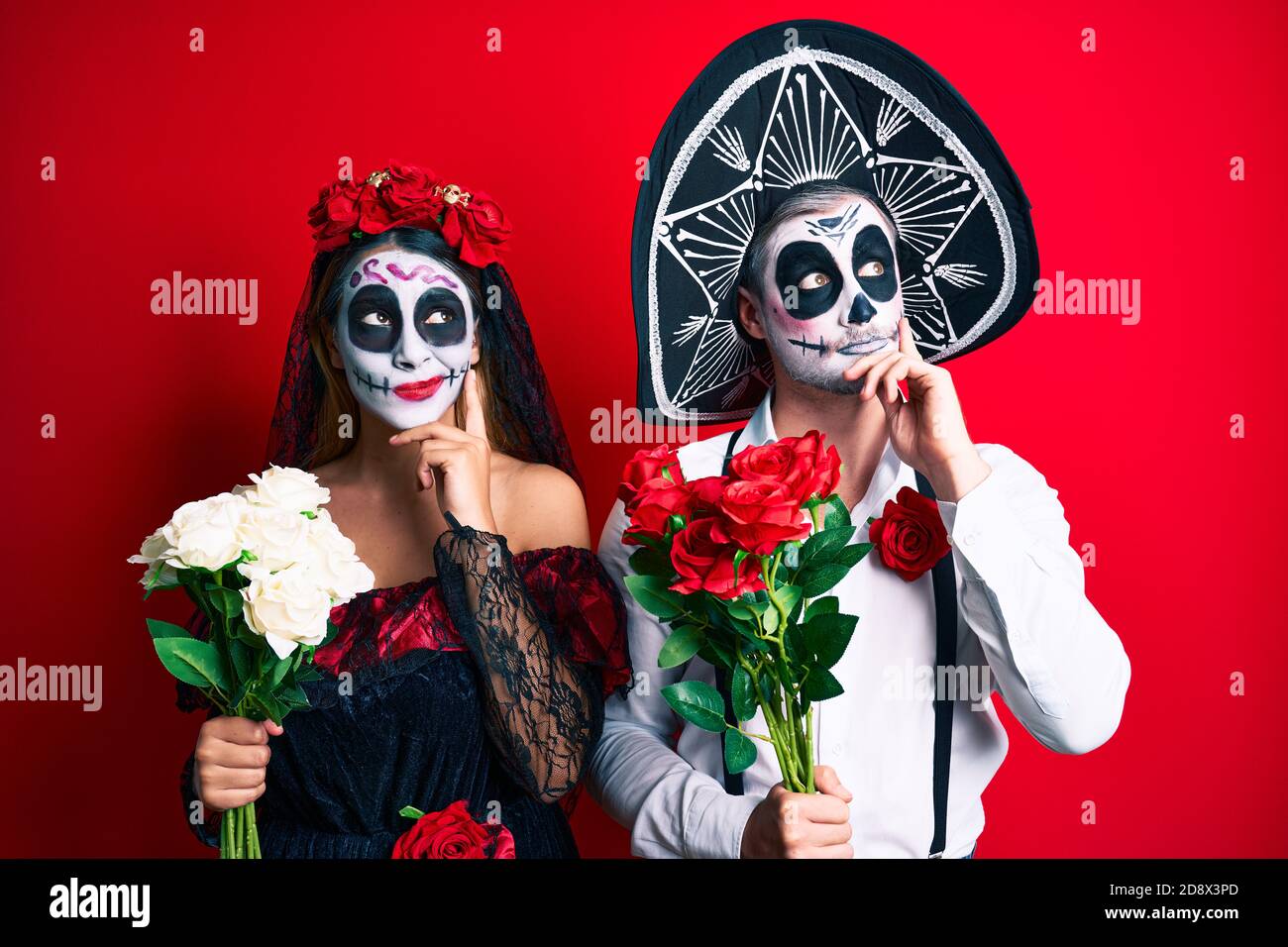 Couple wearing day of the dead costume holding flowers serious face ...