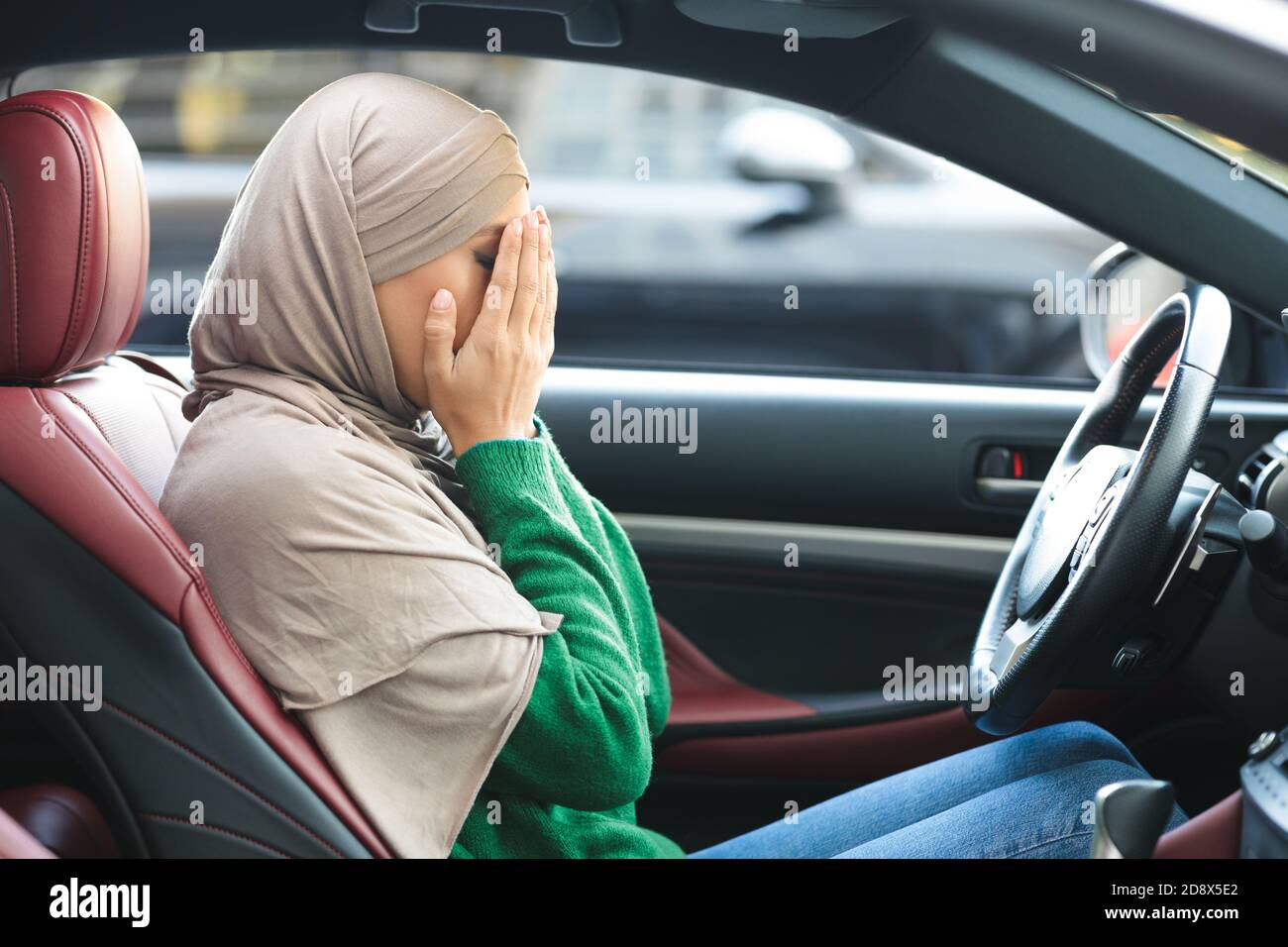 Sad muslim woman driving her car, crying, covering face Stock Photo