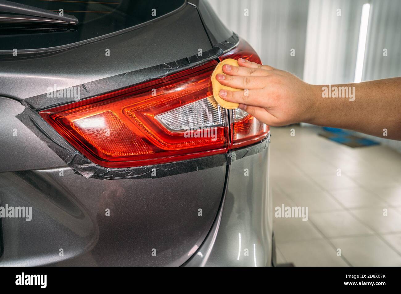 Worker hand polishes headlight with sponge and wax polish paste