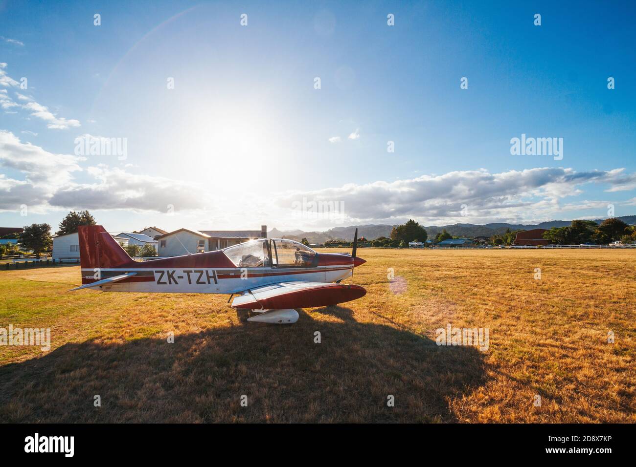 a Robin 2120 two-seater light aircraft sits parked on the grass at Pauanui Airfield, Coromandel, New Zealand as the summer sun sets Stock Photo
