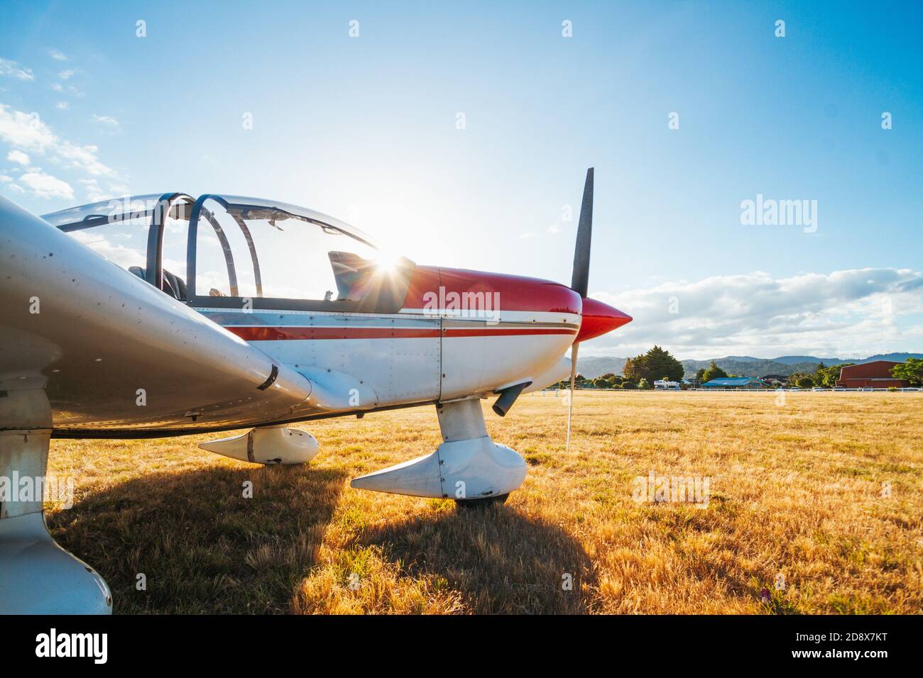 a Robin 2120 two-seater light aircraft sits parked on the grass at Pauanui Airfield, Coromandel, New Zealand as the summer sun sets Stock Photo