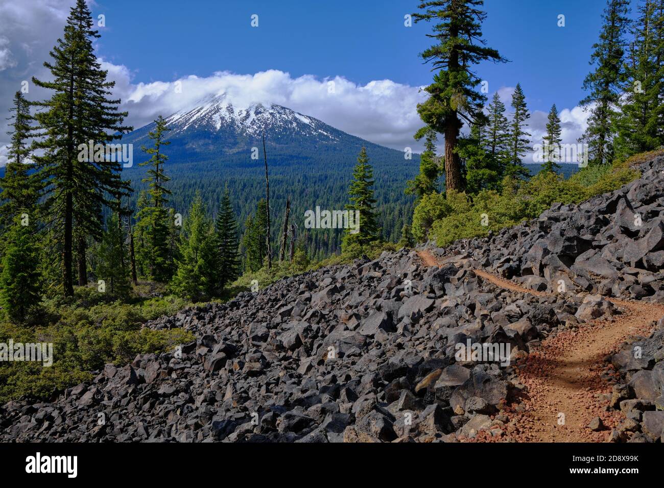 Pacific Coast Trail winding through lava fields in southern Oregon rewards with splendid views of Mount McLoughlin, topped with snow and cloud Stock Photo