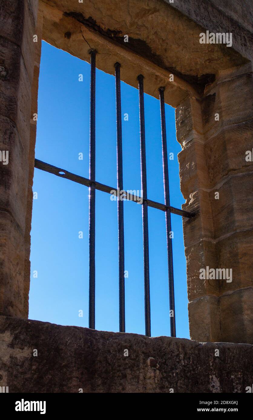 Old sandstone gaol cell (jail cell) with one missing window bar against blue sky Stock Photo