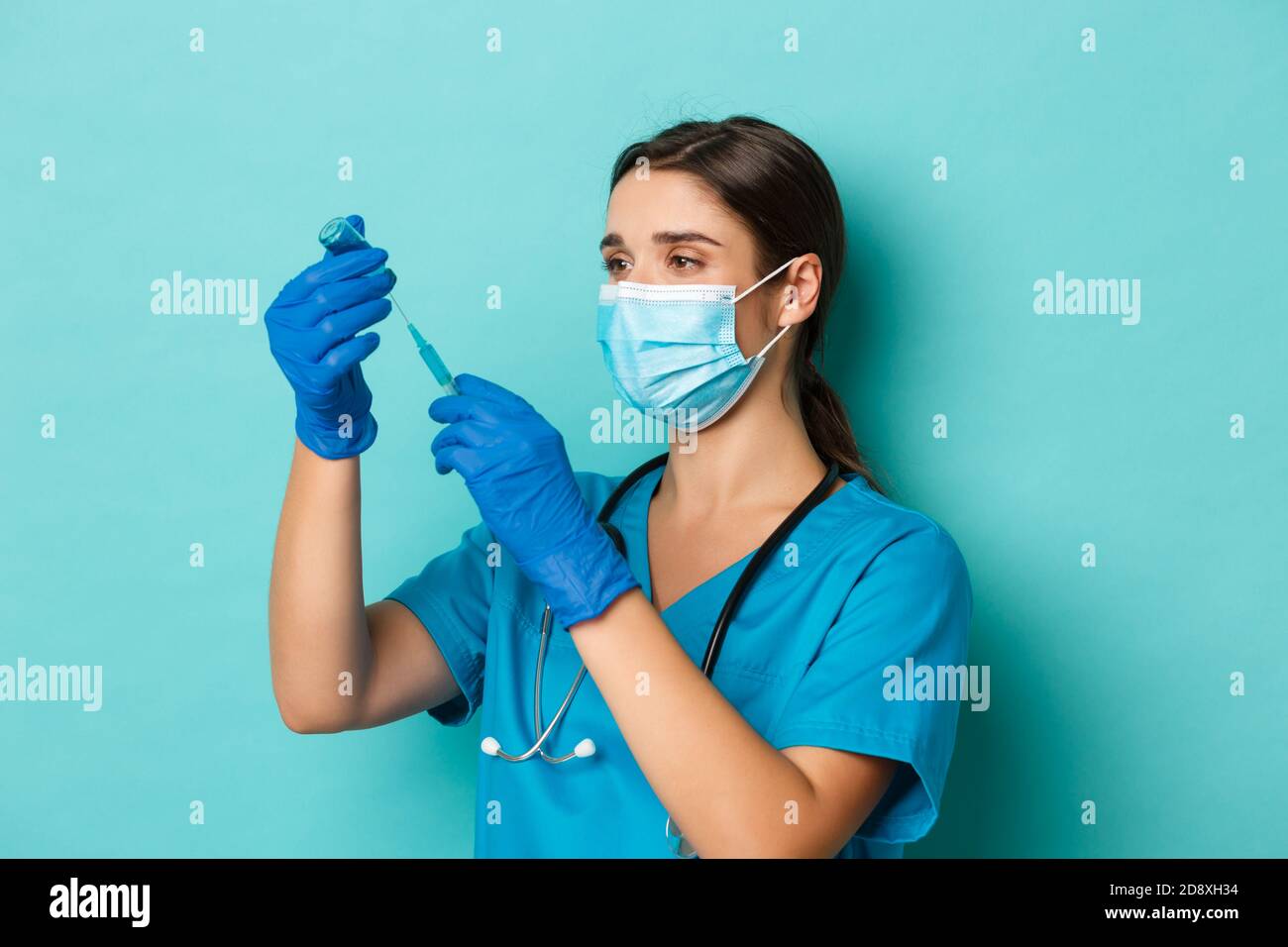 Concept of covid-19 and quarantine concept. Image of female doctor in medical mask, gloves and scrubs, filling syringe with coronavirus vaccine Stock Photo