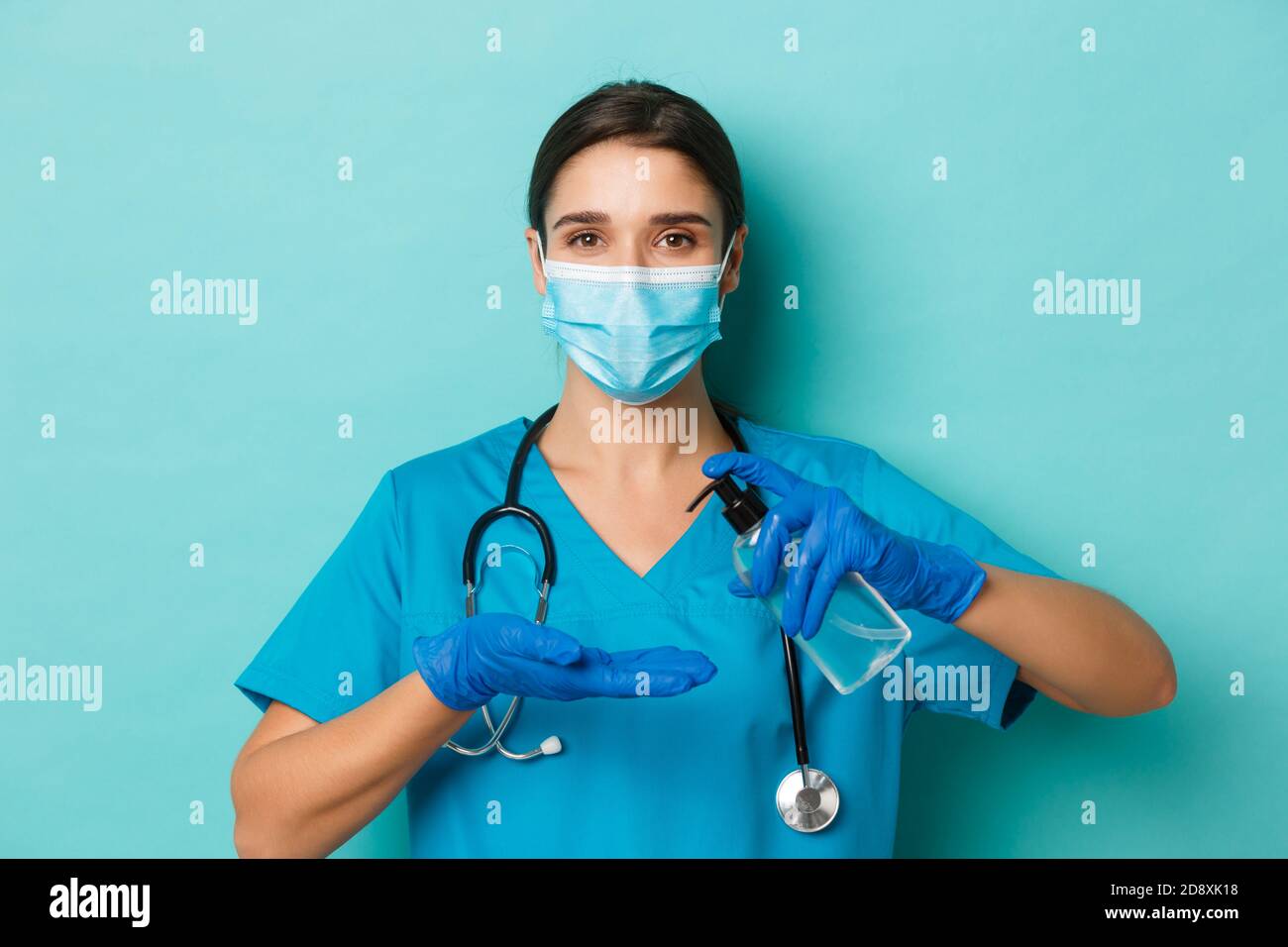 Concept of covid-19 and quarantine concept. Close-up of beautiful female doctor in medical mask, gloves and scrubs, using hand sanitizer, standing Stock Photo