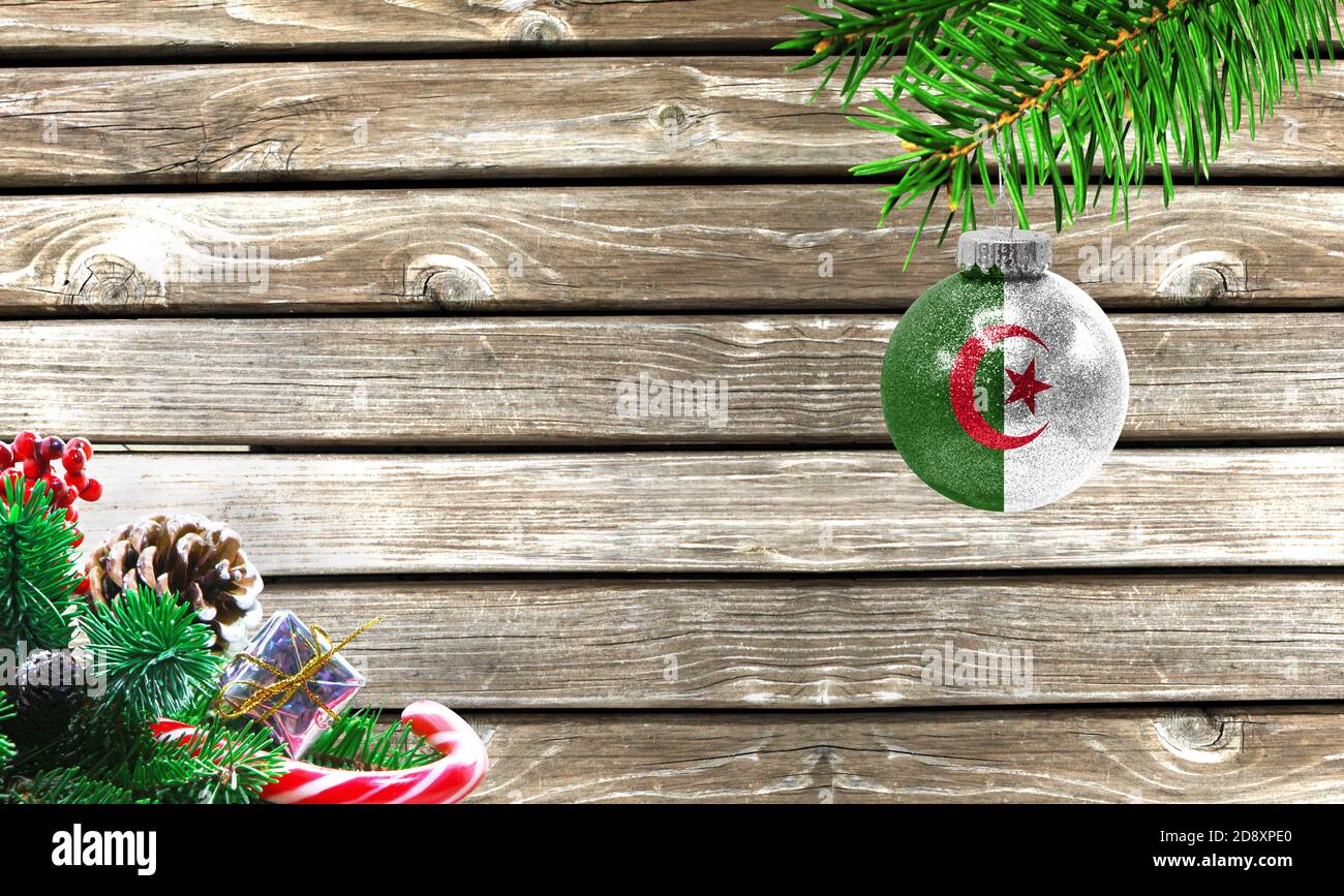 Concept of New Year and Christmas, on a wooden background, Christmas tree branches and a Christmas toy with the flag of Algeria. Stock Photo