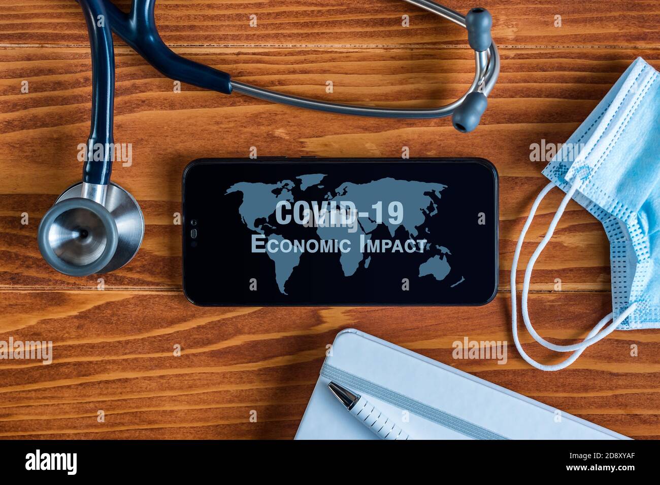 Coronavirus COVID-19 concept: a smartphone sorrounded by a stethoscope, a medical mask and other objects with a world map and an Economic Impact text Stock Photo