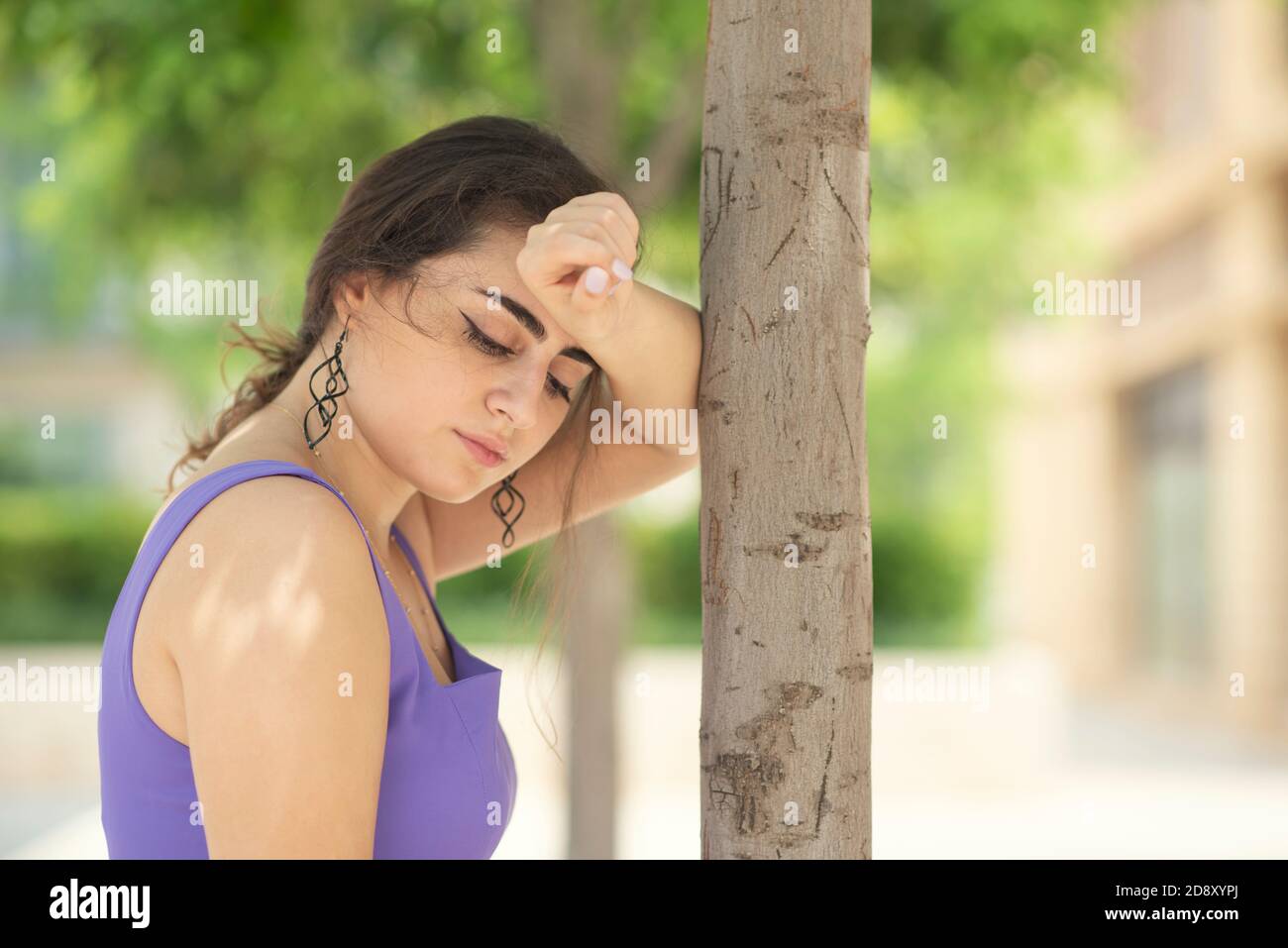 Sad woman leaning against tree Stock Photo