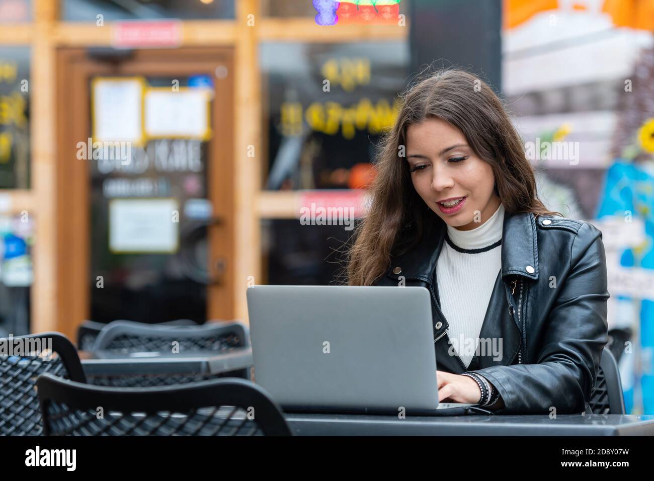 portrait of smart young woman with notebook working on laptop at outdoor coffee shop, work from anywhere concept Stock Photo