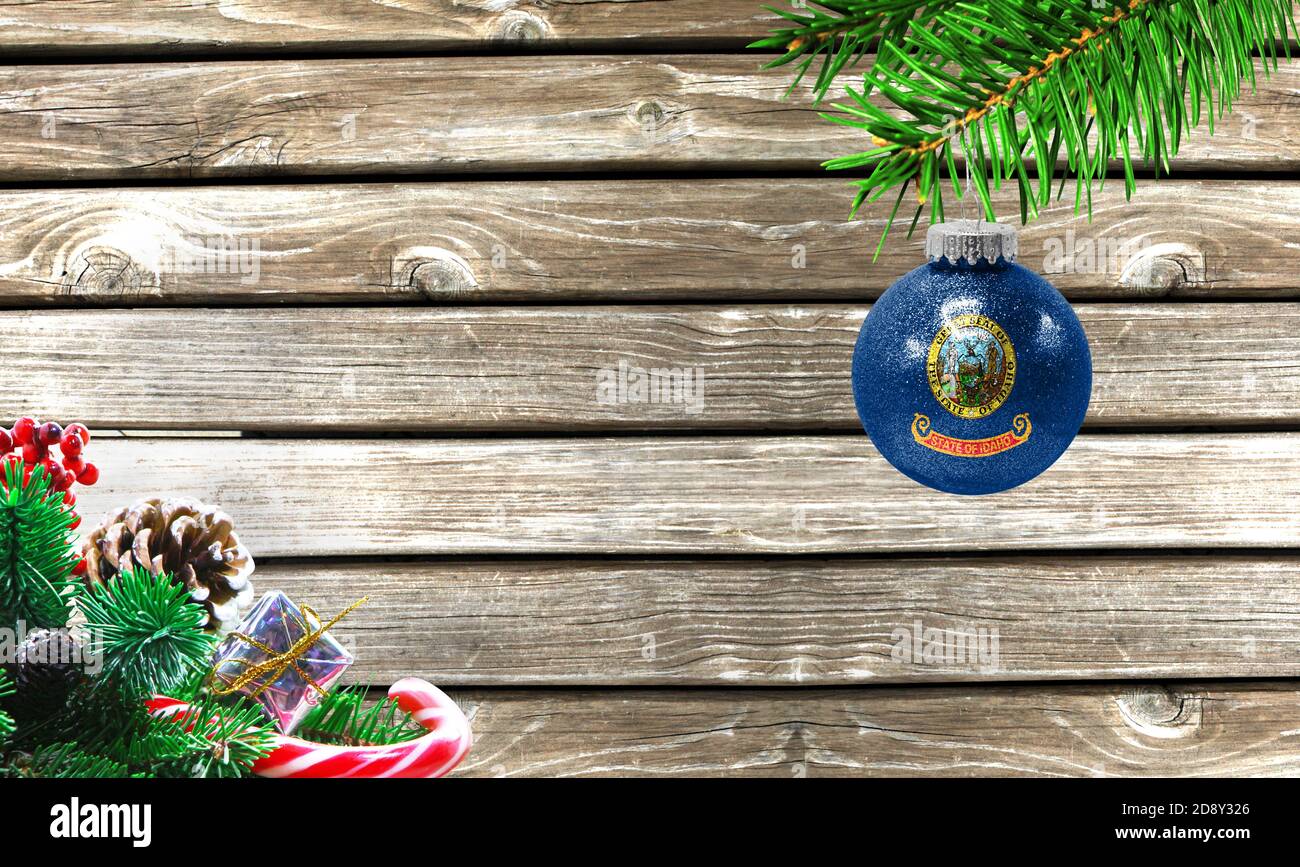 Concept of New Year and Christmas, on a wooden background, Christmas tree branches and a Christmas toy with the flag State of Idaho. Stock Photo