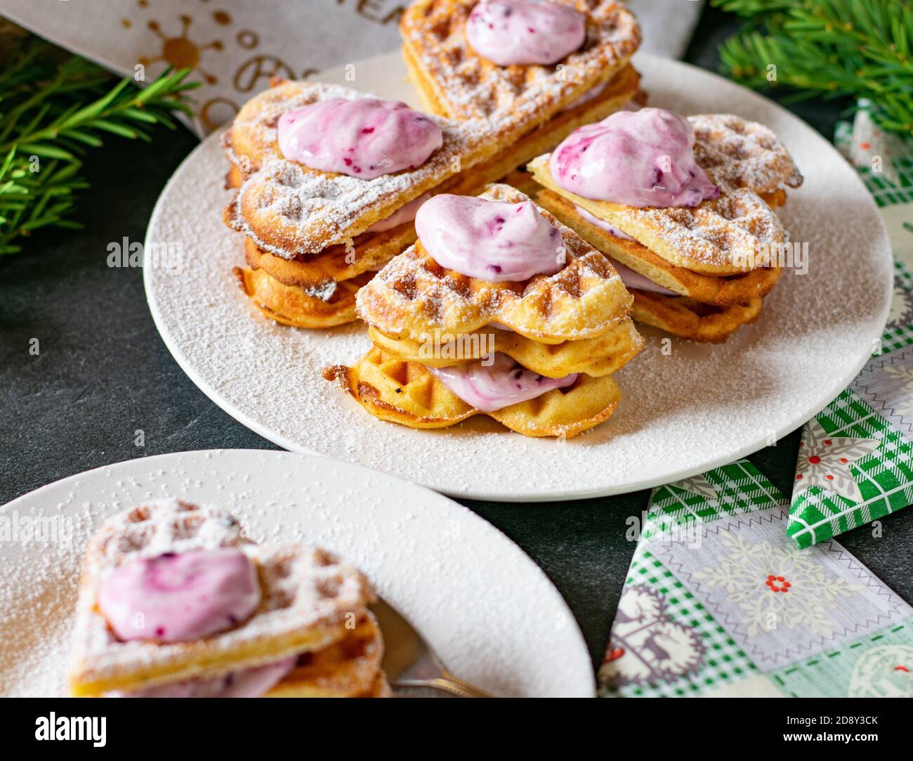 freshly baked waffles in a heart shape served on a plate during christmas with blueberry cream filling and topping Stock Photo