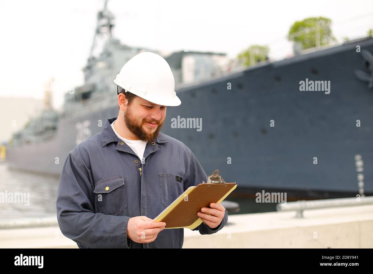 Marine deckhand talking reading documents and standing near vessel. Stock Photo