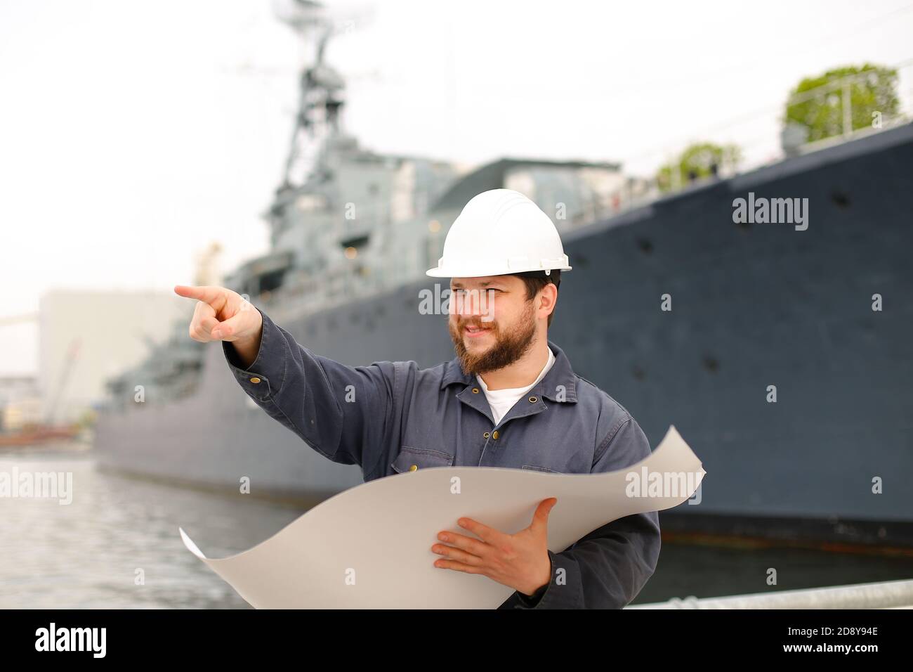Maritime engineer reading blueprints, showing by forefinger and standing near vessel. Stock Photo