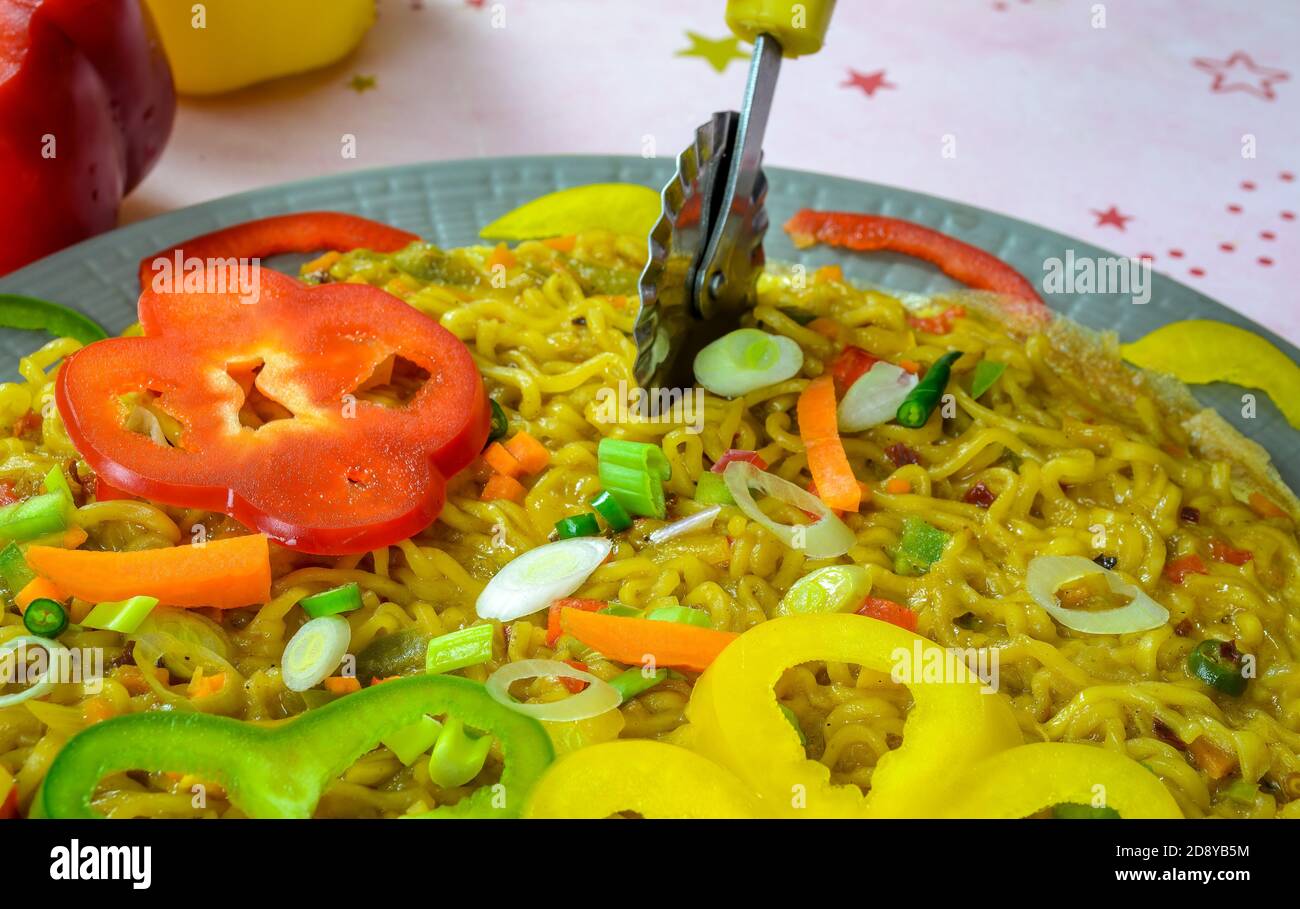 Using pizza cutter to slice a delicious Noodles Omelette garnished with colorful sliced capsicums Stock Photo