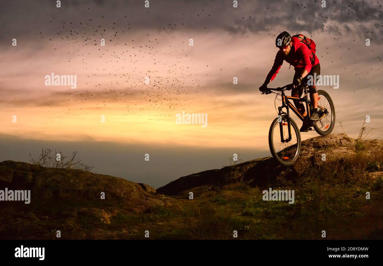 Cyclist in Red Riding Bike on the Autumn Rocky Trail at Sunset. Extreme Sport and Enduro Biking Concept. Stock Photo