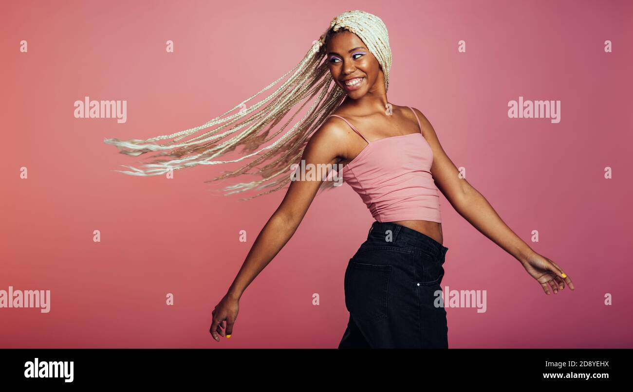 African american woman having long braided hair looking over her shoulder. Smiling woman flying her hair around on pink background. Stock Photo
