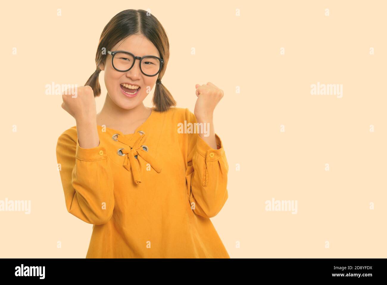 Studio shot of young happy Asian woman cheering with both arms raised Stock Photo