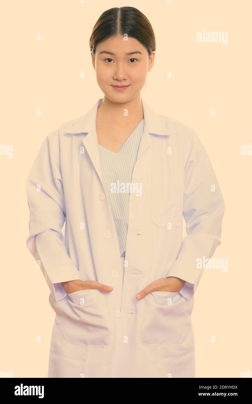 Studio shot of young beautiful Asian woman doctor standing with hands ...