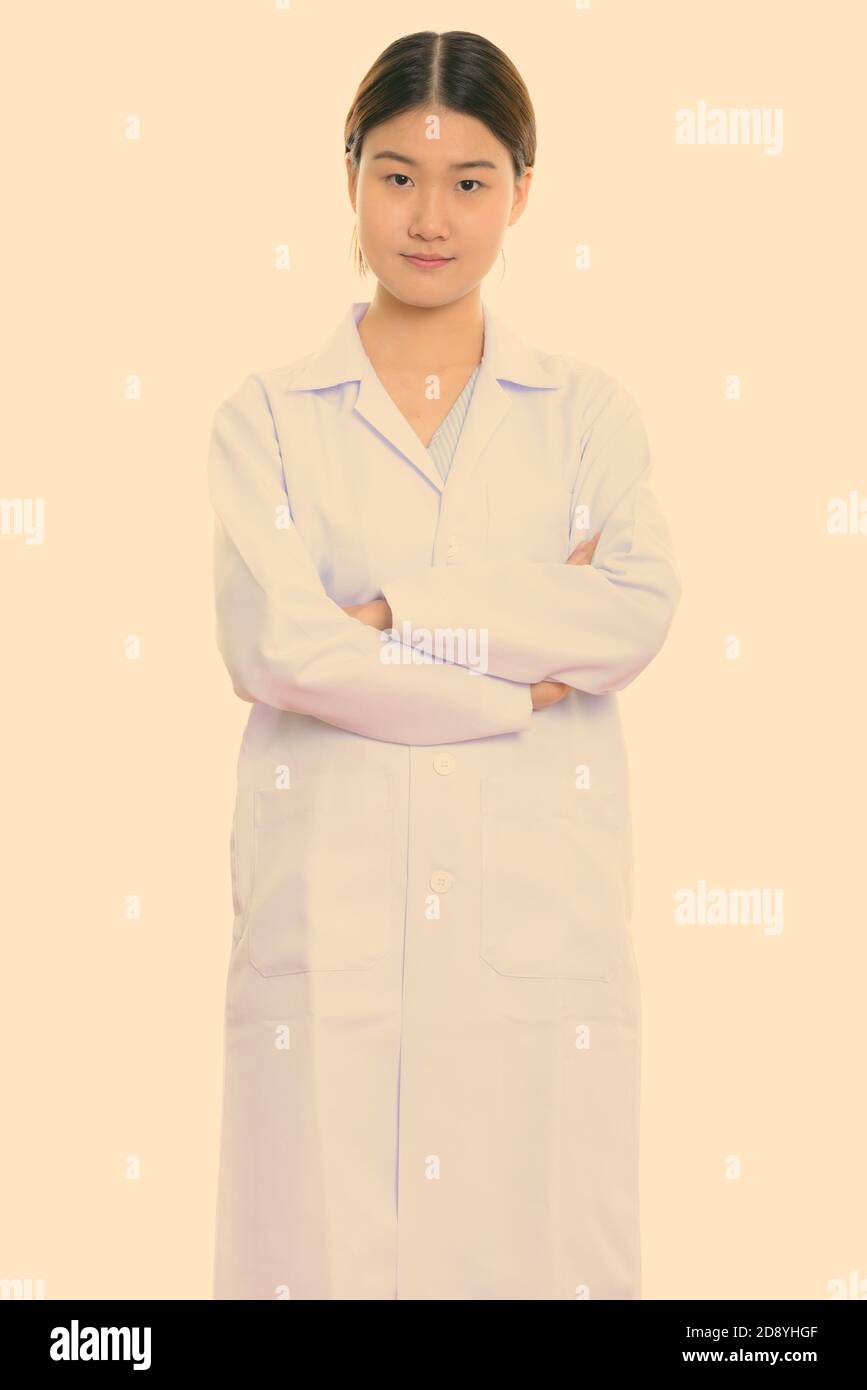 Studio shot of young beautiful Asian woman doctor standing with arms ...