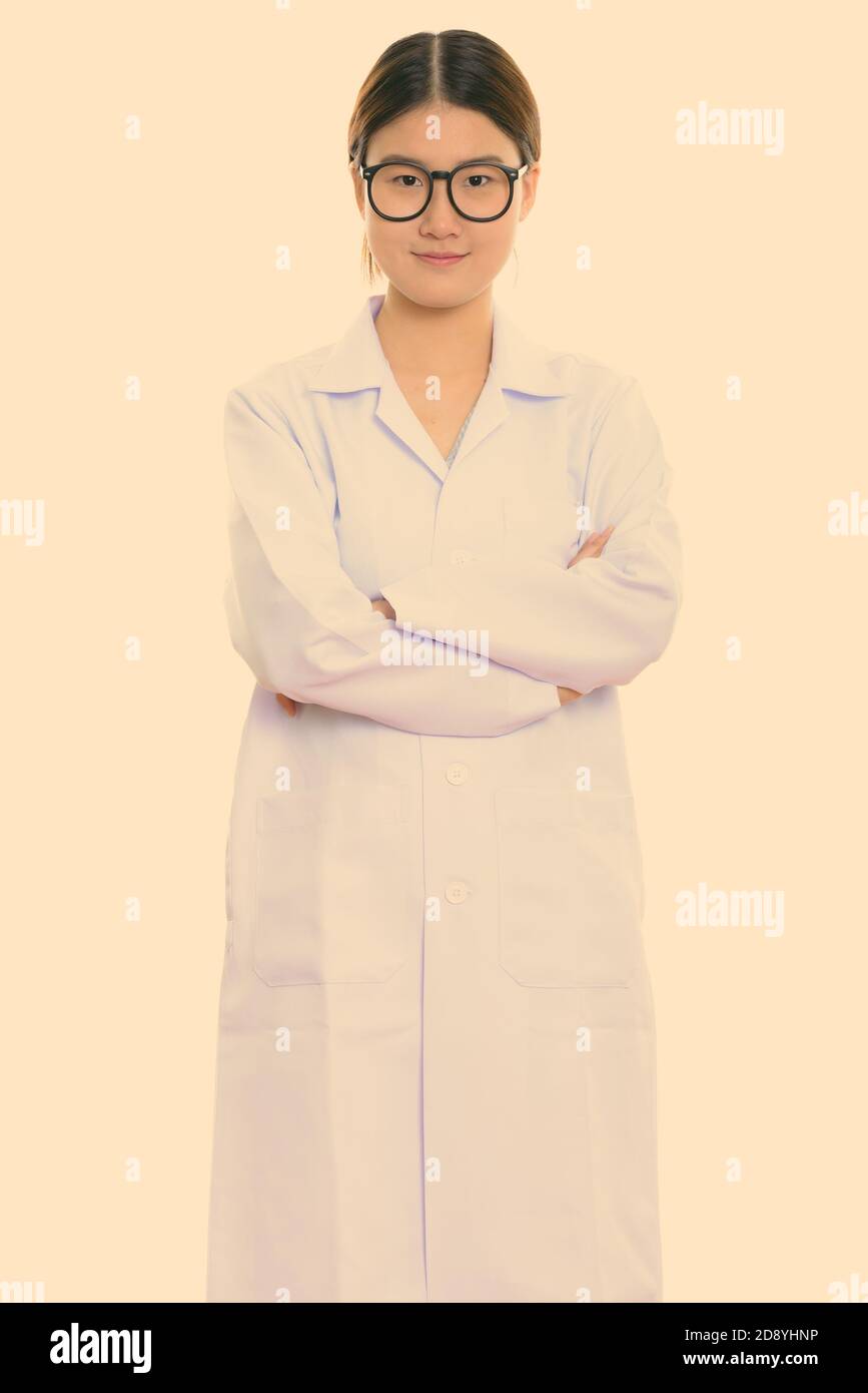 Studio shot of young beautiful Asian woman doctor standing with arms ...