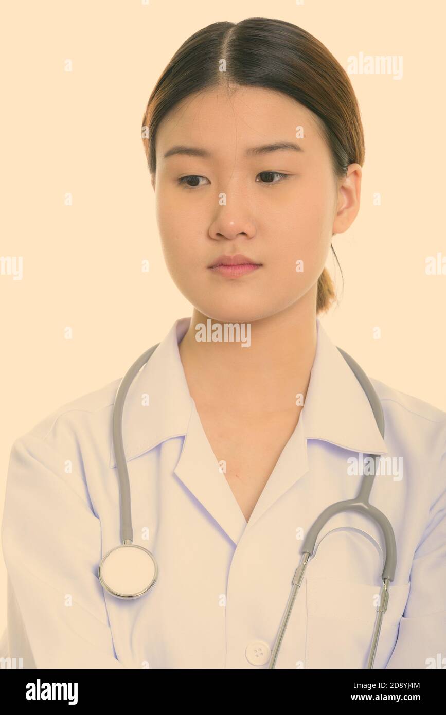 Studio shot of young beautiful Asian woman doctor thinking while ...