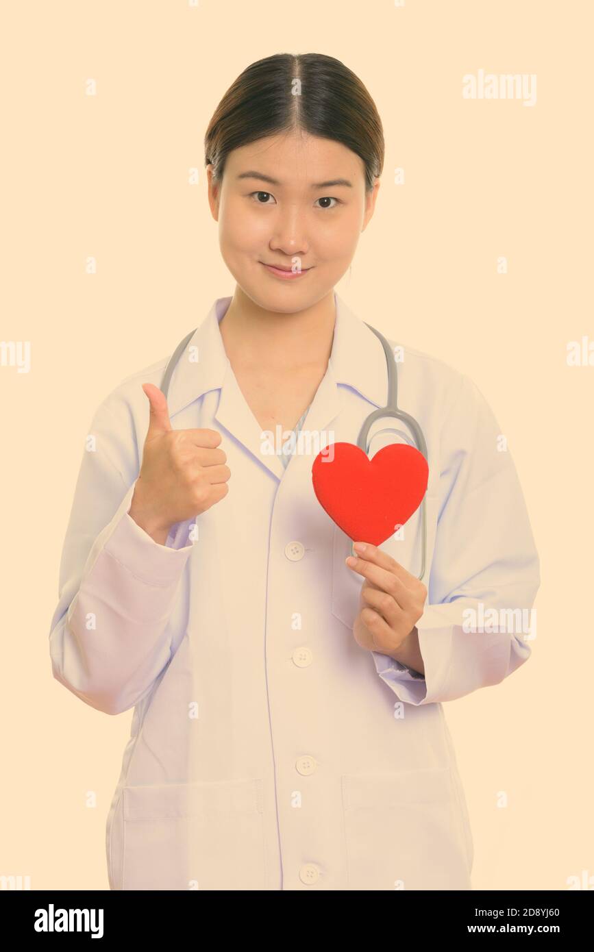 Young beautiful Asian woman doctor holding red heart and giving thumb ...