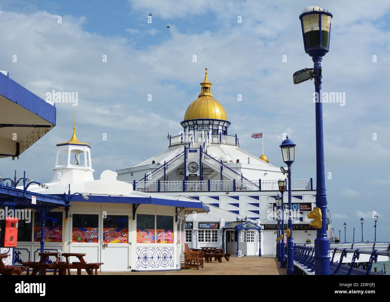 Open deck of Eastbourne pier with seating and arcade entertainment. Gold dome of the pier's tower shines in the sunlight. Stock Photo