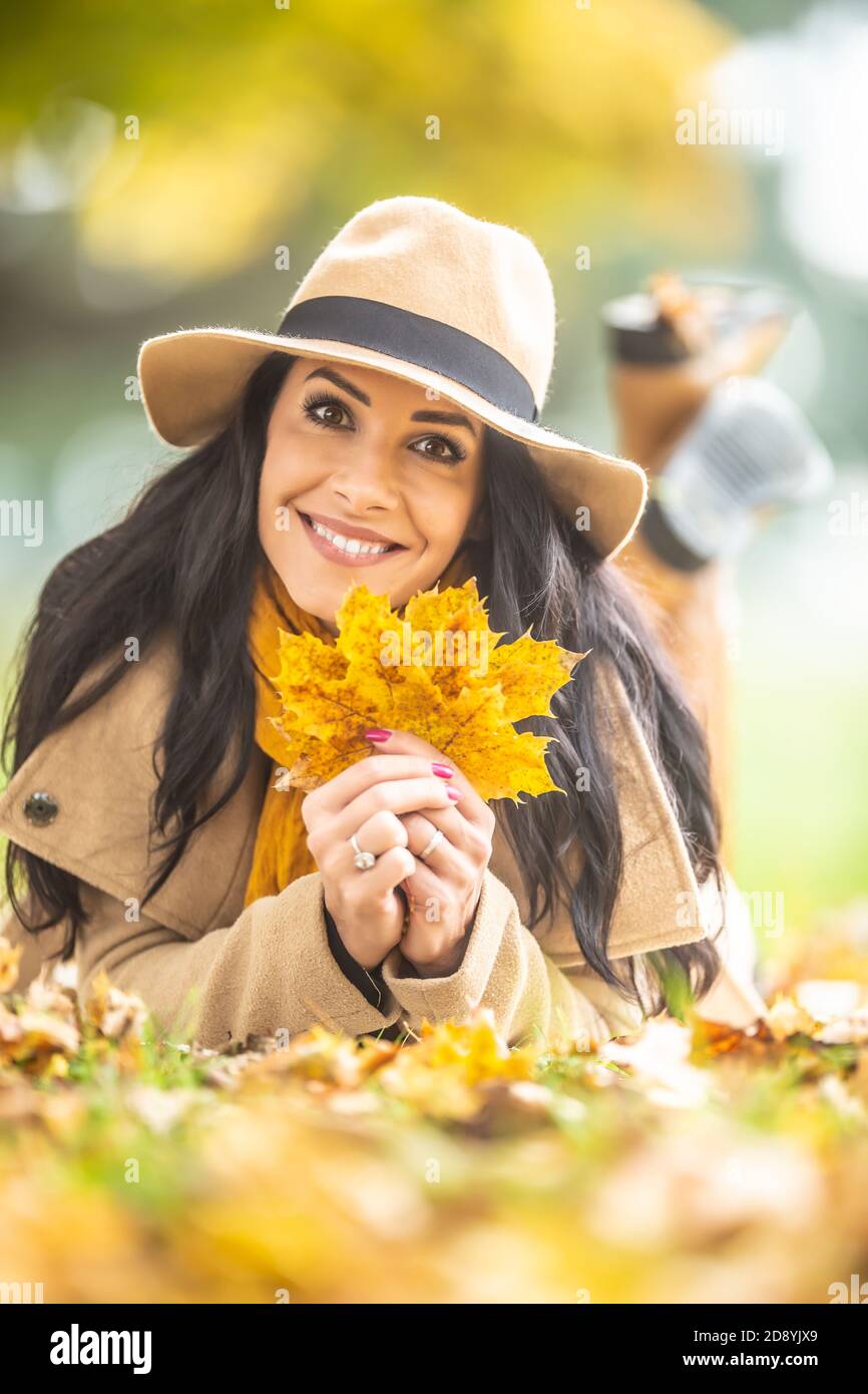 Hat wearing beauty holds maple leaves smiling at the camera Stock Photo ...
