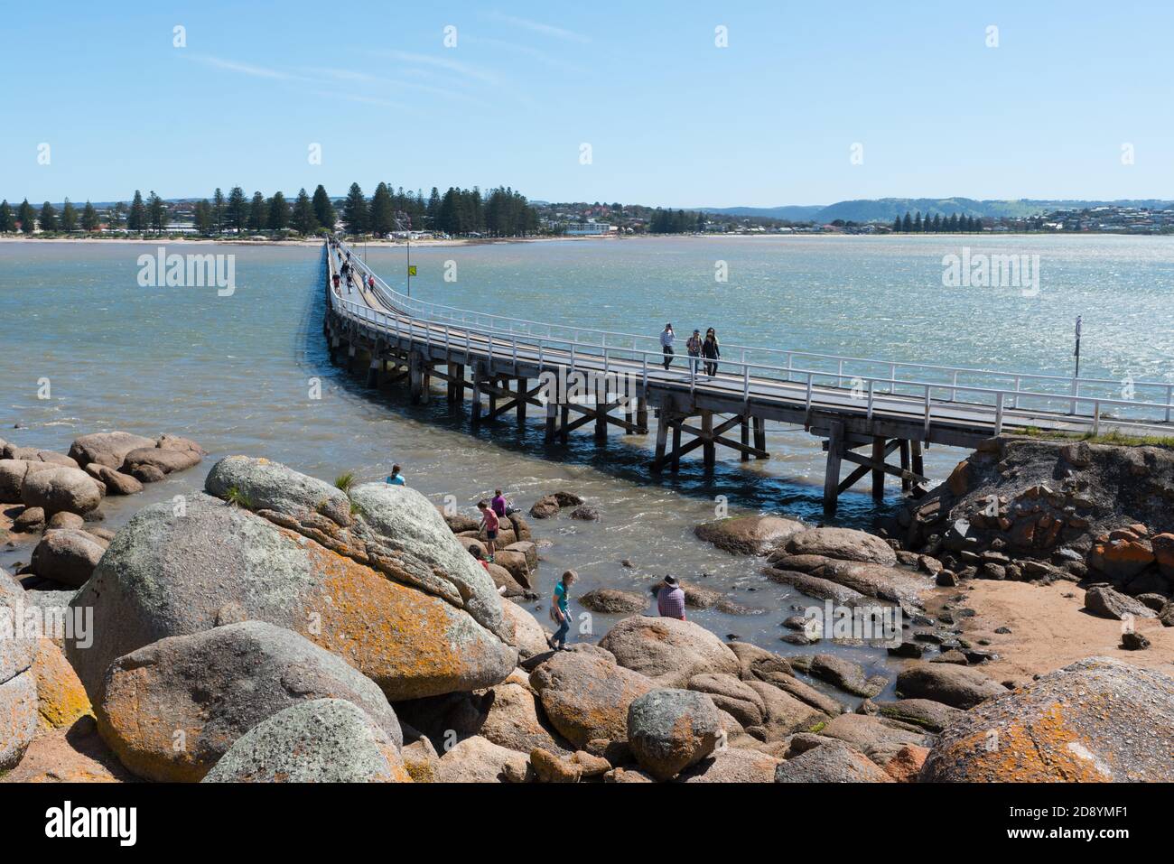 Children playing in the water while families walk on the causeway bridge from Victor Harbor to Granite Island in South Australia Stock Photo