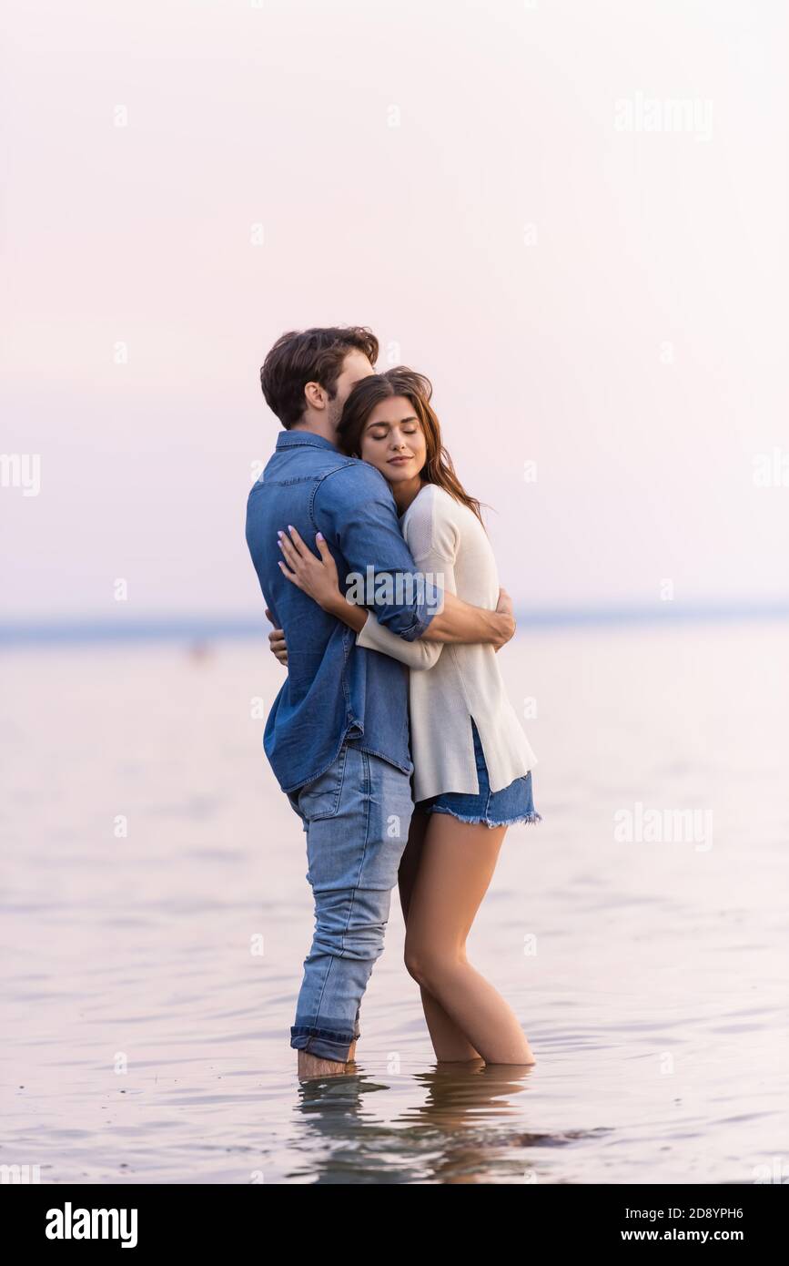 Side view of brunette woman with closed eyes hugging boyfriend while ...