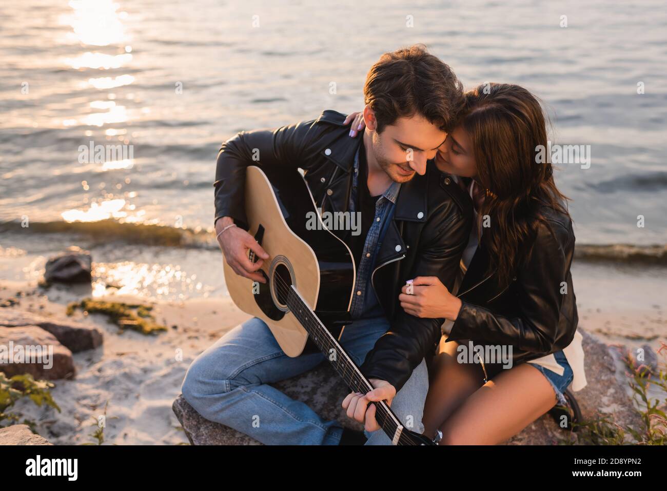 Brunette woman hugging boyfriend in leather jacket with acoustic guitar ...
