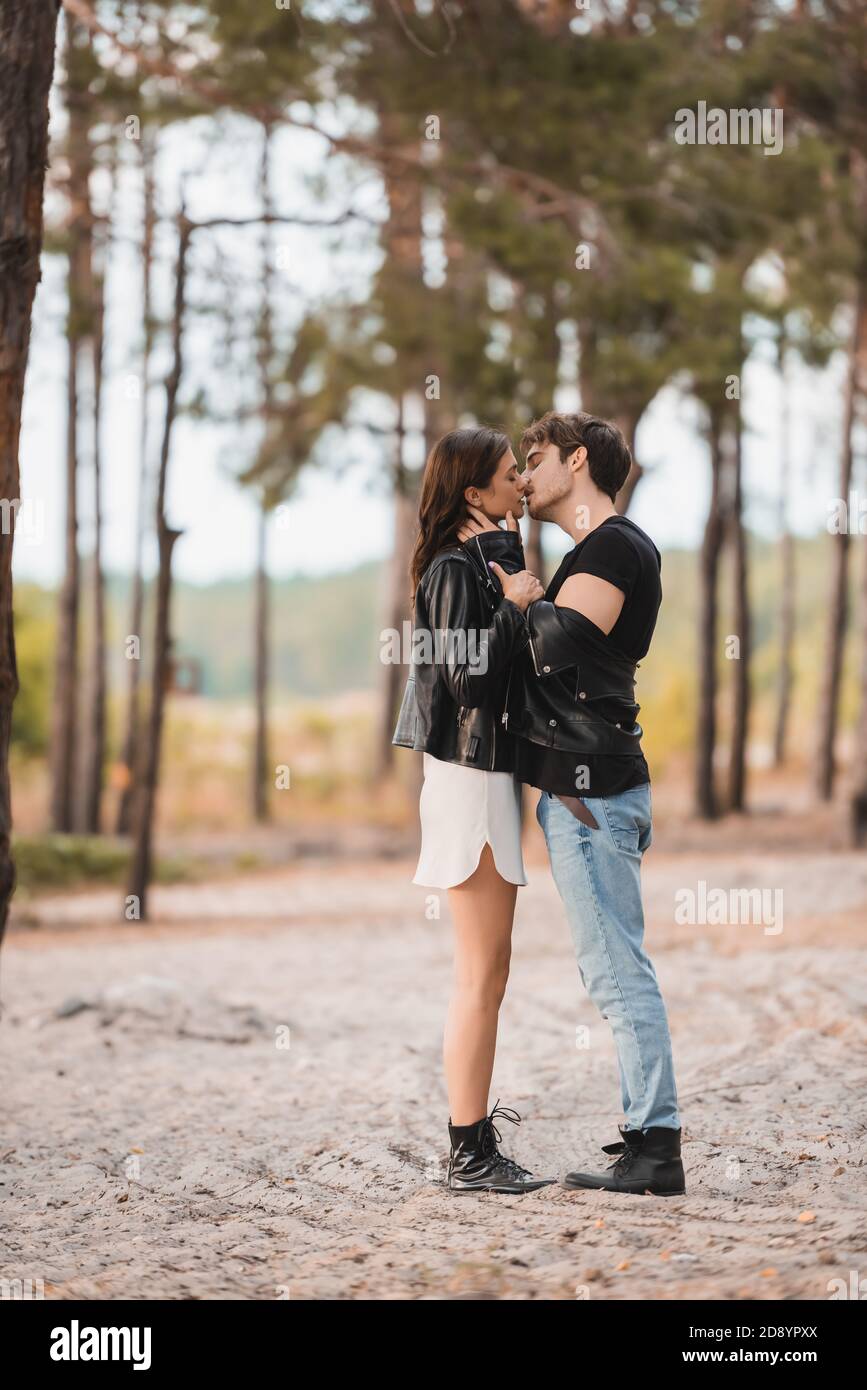 Side view of man in leather jacket kissing brunette girlfriend on sand ...
