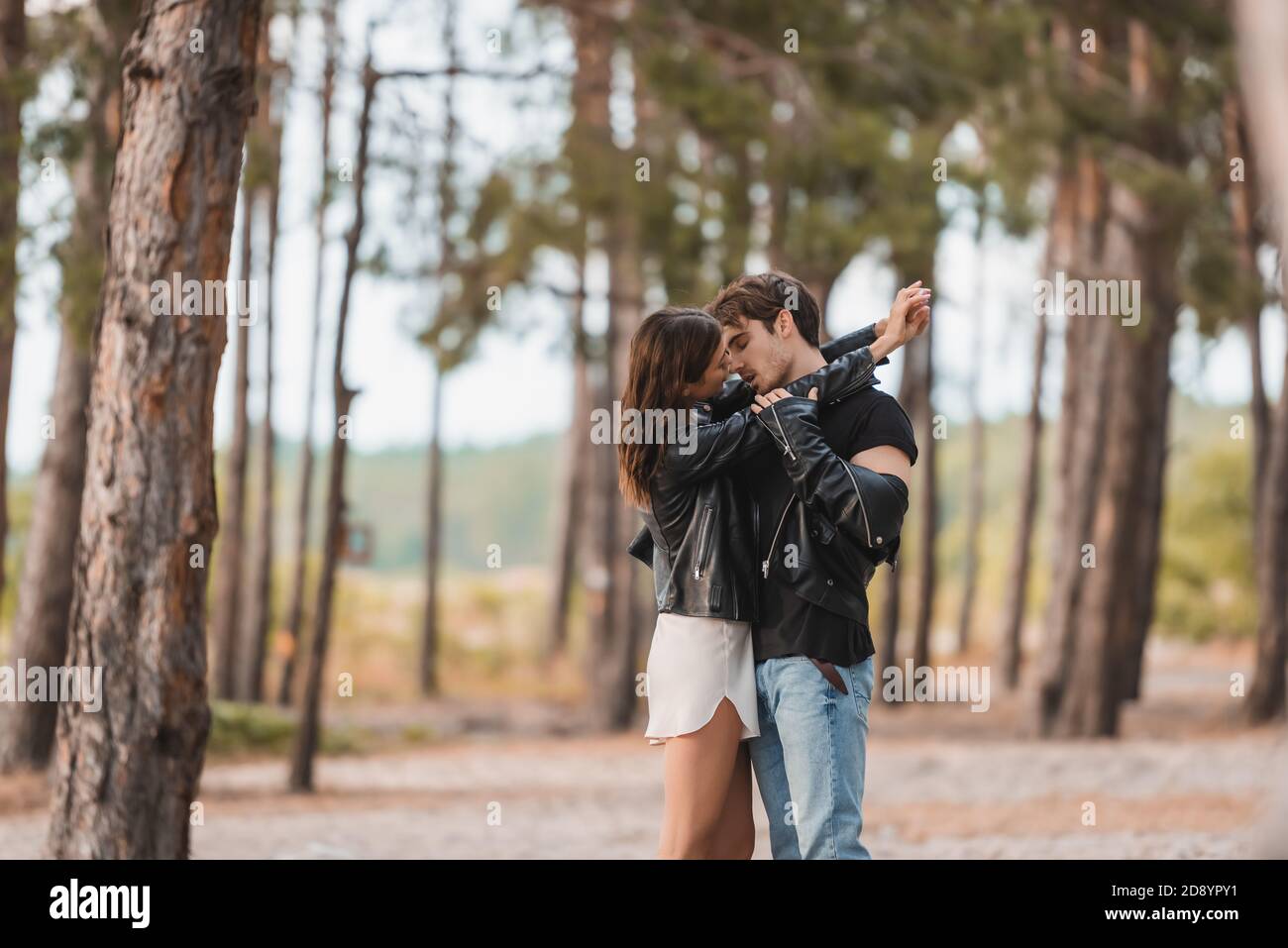 Selective focus of young couple in leather jackets kissing in forest ...