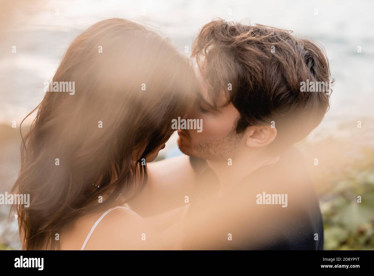 Selective focus of young man kissing brunette woman near sea Stock Photo photo