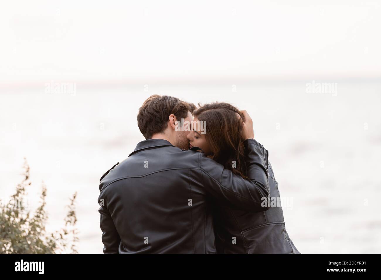 Back view of young couple in leather jackets kissing near sea Stock ...