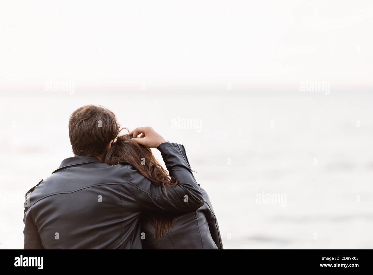 Back view of man in leather jacket touching hair of girlfriend near sea ...