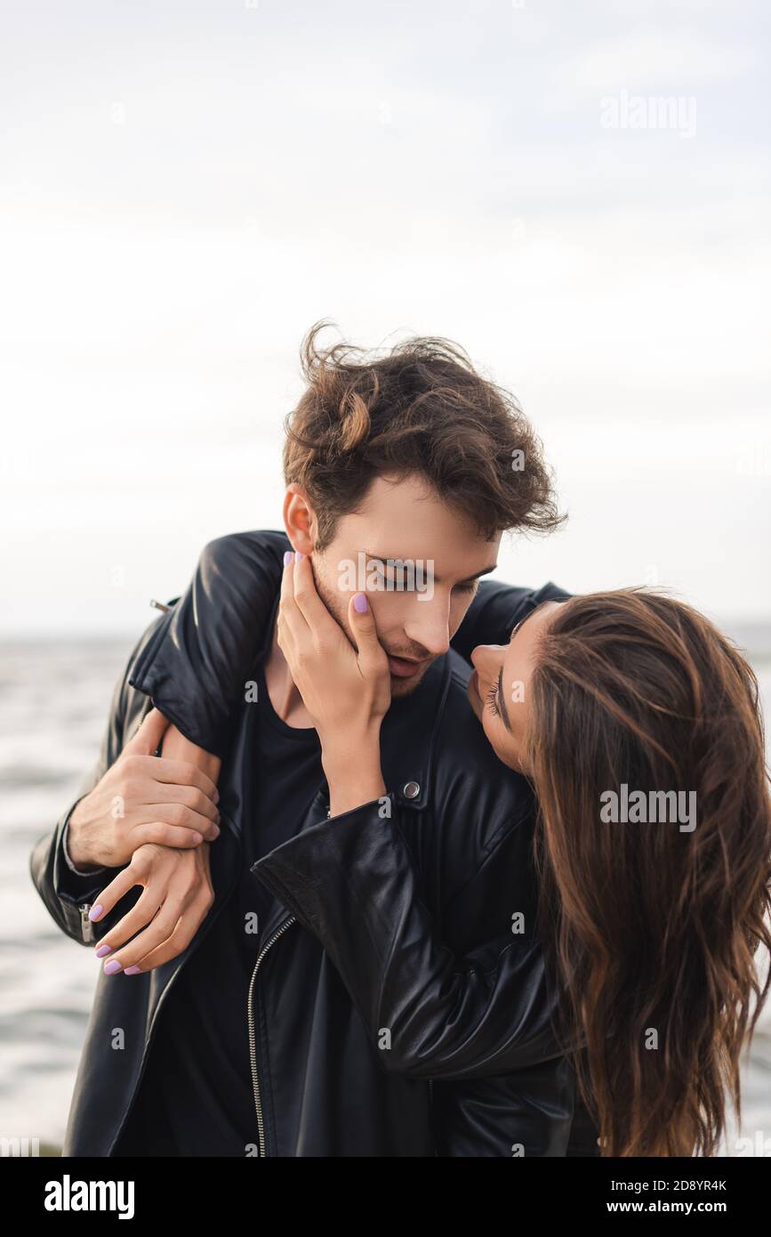 Young woman touching cheek and embracing boyfriend in leather jacket ...