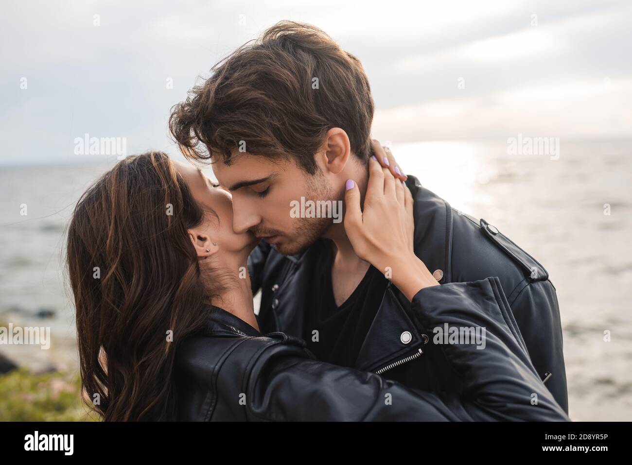Young woman touching neck of boyfriend in leather jacket on beach Stock ...
