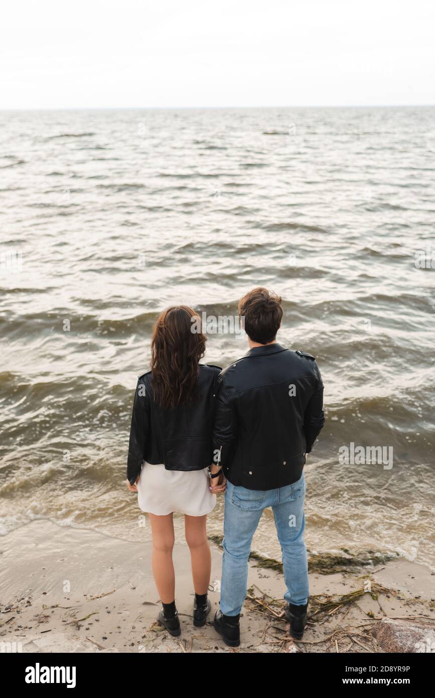 Back view of man in leather jacket standing near girlfriend on beach ...