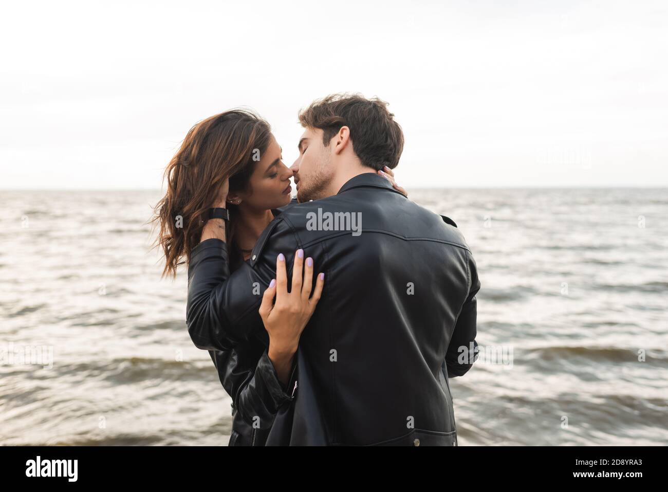 Man in leather jacket kissing girlfriend with sea at background Stock ...