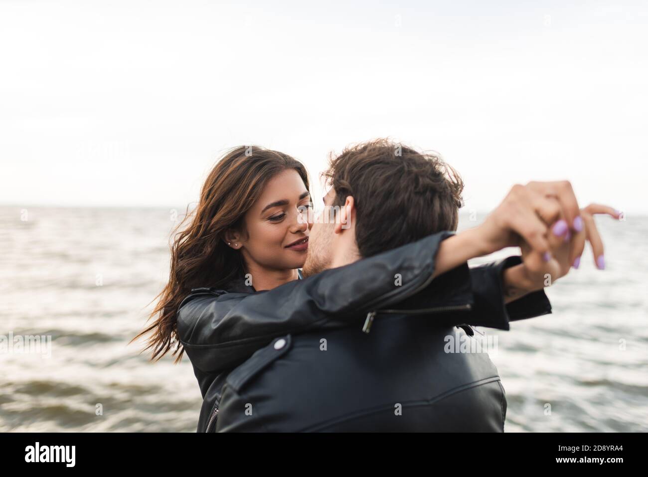 Man in leather jacket kissing woman near sea Stock Photo - Alamy