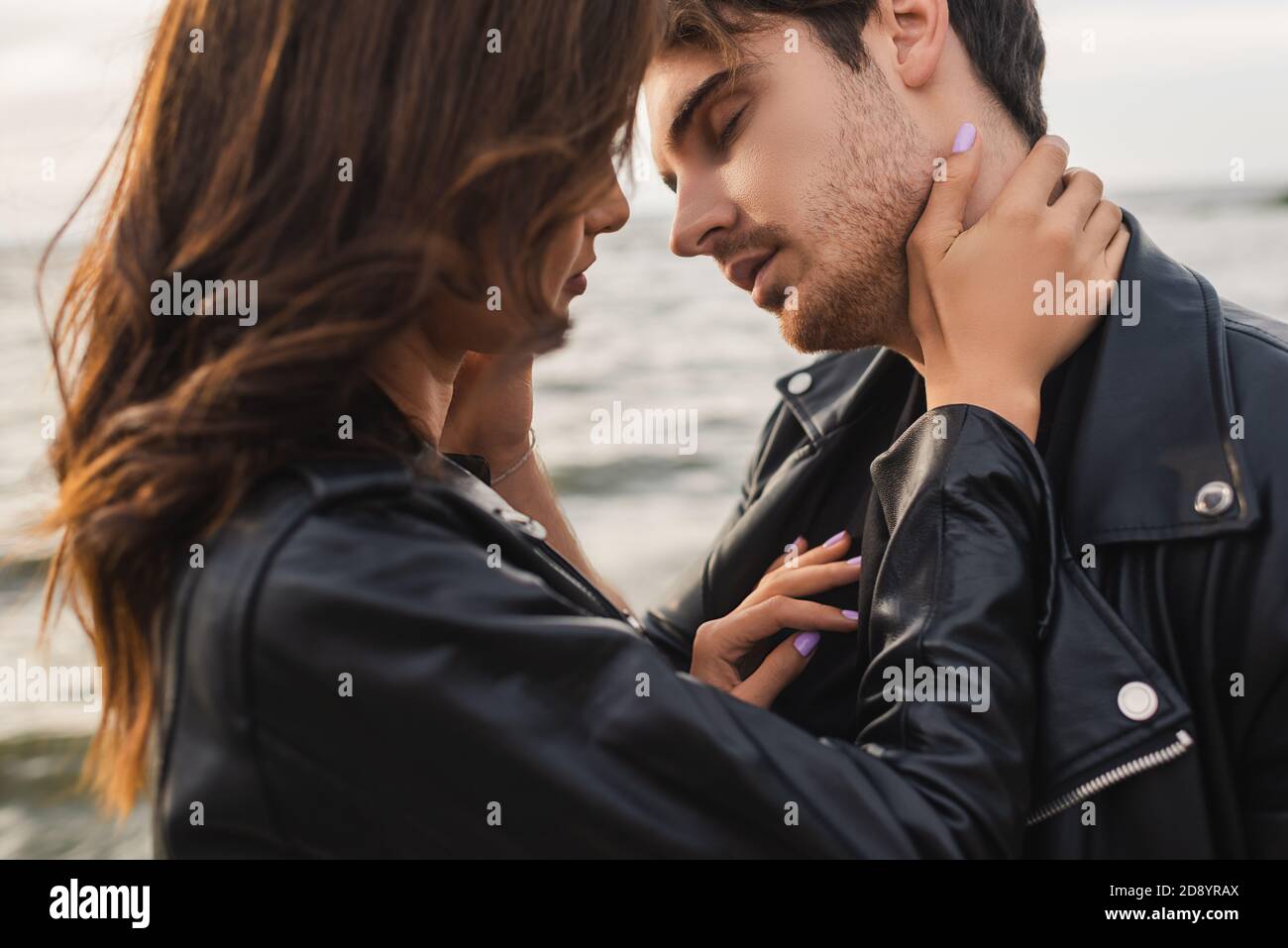 Young woman touching neck of boyfriend in leather jacket near sea Stock ...