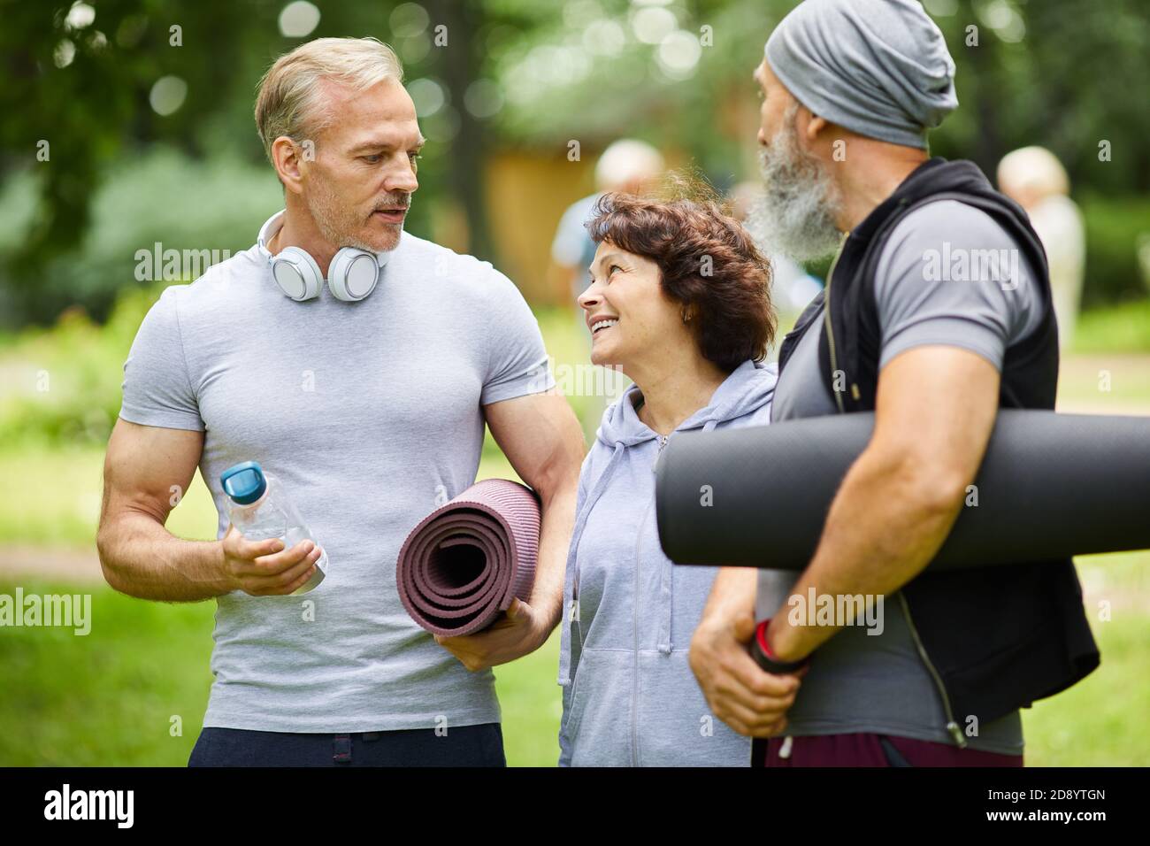 Two sporty mature men and woman standing together in park discussing something before doing exercise Stock Photo