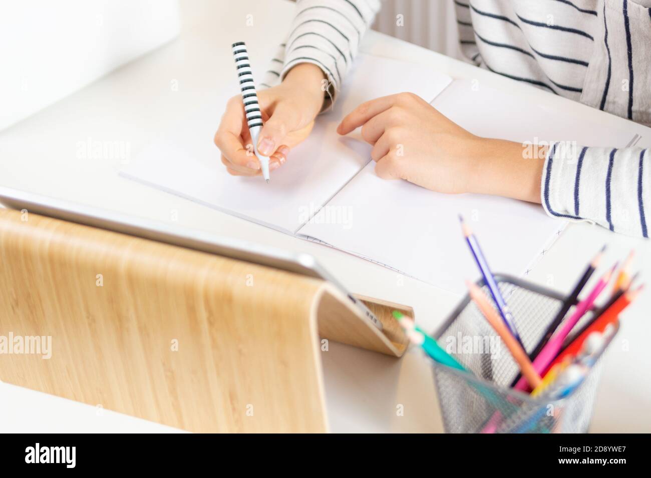 Close up of kid hands writing homework in notebook with pen. Child sitting at table with digital tablet computer at home Stock Photo