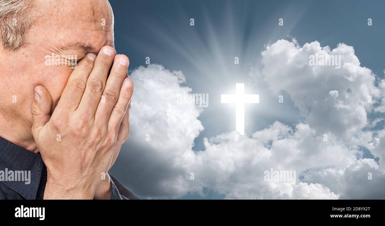 Elderly man with a face closed by hands on the background of the sky with a cross, a symbol of faith Stock Photo