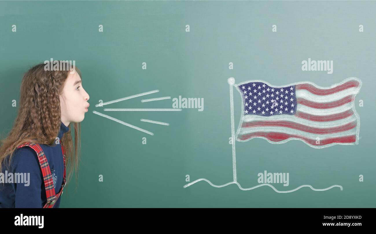 Pre-adolescent girl blowing on the school board drawn on the blackboard American flag. High resolution photo. Full depth of field. Stock Photo
