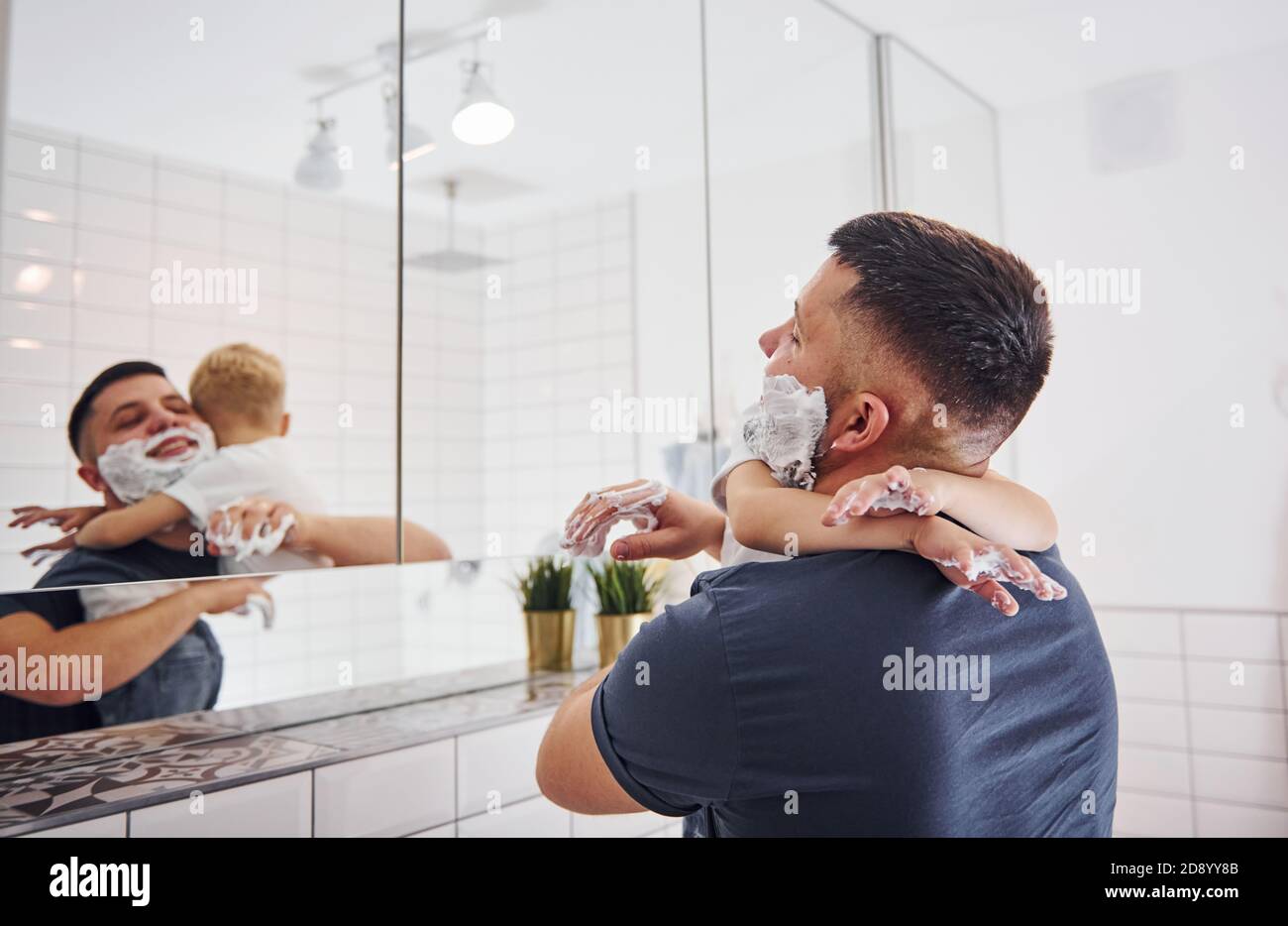 Father with his son is in the bathroom have fun by using shaving gel and looking in the mirror Stock Photo